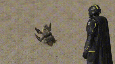 A Superhero In A Black Cape And Helmet Is Standing Next To A Toy Robot . GIF