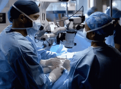 A Surgeon Is Looking Through A Microscope While Another Surgeon Looks On GIF