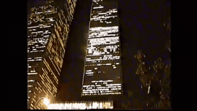 A Tall Building Is Lit Up At Night With A Street Light In The Foreground GIF