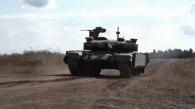 A Tank Is Driving Down A Dirt Road In A Field . GIF