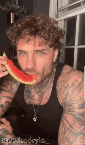 A Tattooed Man Is Eating A Slice Of Watermelon With The Hashtag Declardoyle GIF