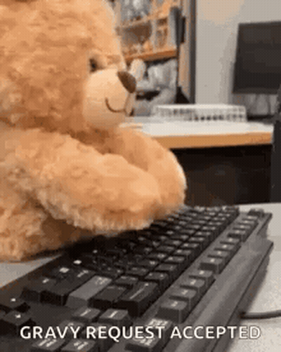 A Teddy Bear Is Sitting At A Desk Typing On A Computer Keyboard . GIF