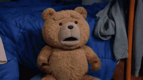 A Teddy Bear Is Sitting On A Bed With Its Mouth Open GIF