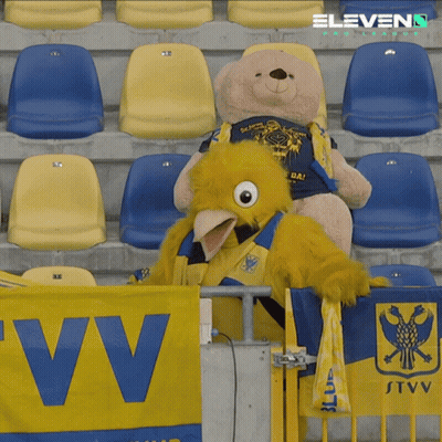 A Teddy Bear Sits Next To A Mascot In A Stadium GIF