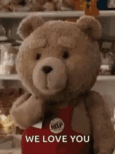 A Teddy Bear Wearing A Red Apron Is Standing In Front Of A Refrigerator . GIF