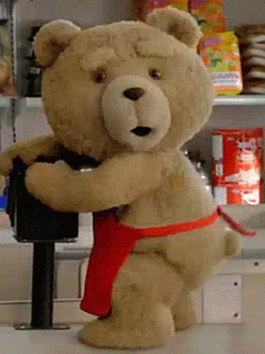 A Teddy Bear Wearing A Red Apron Is Standing On A Counter In A Store GIF