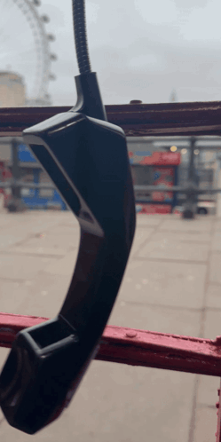 A Telephone Hanging From A Red Railing With A Ferris Wheel In The Background GIF
