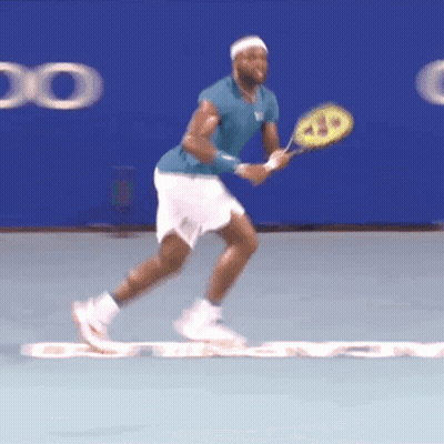 A Tennis Player In A Blue Shirt And White Shorts Holds A Wilson Racquet GIF