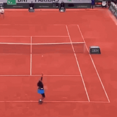 A Tennis Player Is Hitting A Tennis Ball On A Red Tennis Court . GIF