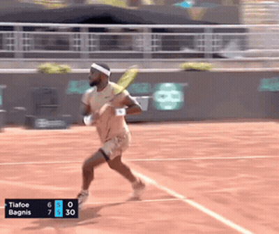 A Tennis Player Is Running On A Court With A Scoreboard That Says Tiafoe Bagnis At The Bottom GIF