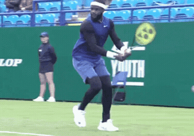 A Tennis Player Is Swinging A Racket In Front Of A Green Wall That Says Dunlop Youth GIF