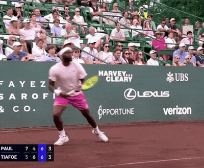 A Tennis Player Is Swinging A Tennis Racquet In Front Of A Green Wall That Says Harvey Cleary On It GIF