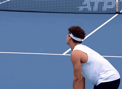 A Tennis Player Reaches For A Tennis Ball On A Court That Has A Lacos Sign On It GIF