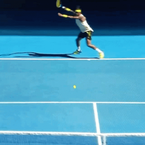 A Tennis Player Swings A Racket At A Yellow Ball On A Blue Court GIF