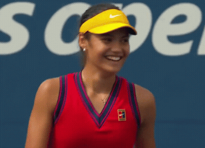A Tennis Player Wearing A Red Tank Top And A Yellow Visor Is Smiling On A Tennis Court . GIF