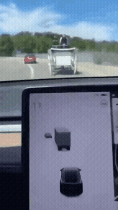 A Tesla Model 3 Is Driving Down A Highway Next To A Truck And A Red Car . GIF