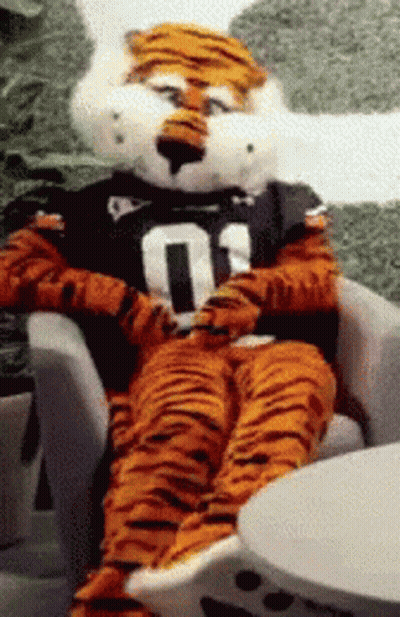 A Tiger Mascot Is Sitting In A Chair Wearing A Number 01 Shirt GIF