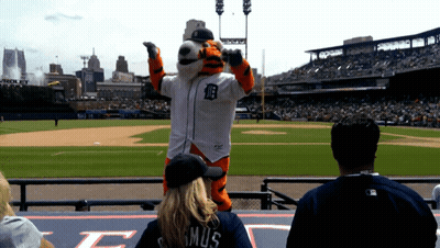 A Tiger Mascot Stands On A Baseball Field With A Woman Wearing A Shirt That Says Mus GIF