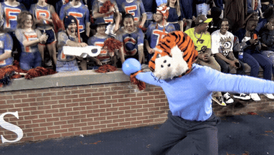 A Tiger Mascot Throws A Blue Ball In Front Of A Crowd With A Letter S In The Background GIF