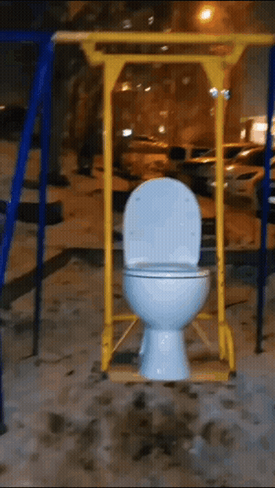 A Toilet On A Swing In A Playground At Night GIF