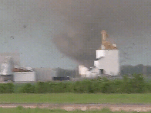 A Tornado Is Coming Towards A Building With Smoke Coming Out Of It GIF