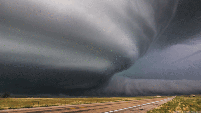 A Tornado Is Moving Over A Dirt Road In The Middle Of A Field GIF