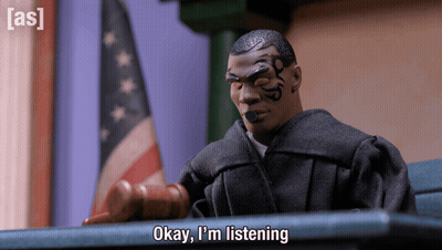 A Toy Judge Says " Okay I 'M Listening " In Front Of A Flag GIF