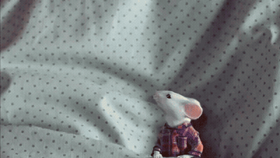 A Toy Mouse Is Sitting On A Bed With Polka Dots GIF