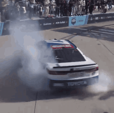 A Toyota Race Car Is Doing A Burnout In Front Of A Crowd GIF