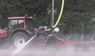 A Tractor With A Hose Attached To It Is Spraying Water On A Car . GIF