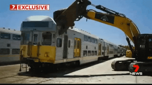 A Train Is Being Demolished By A Yellow Excavator With A Sign That Says Exclusive GIF