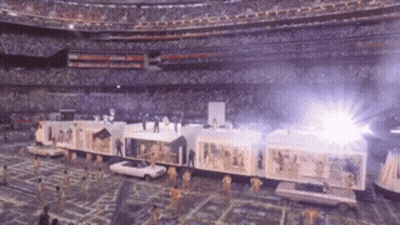 A Train Is Being Pulled By Cars In A Stadium With A Crowd In The Background GIF