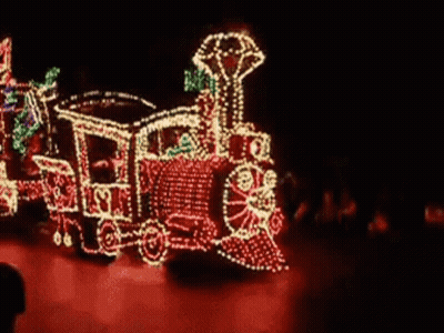 A Train Is Decorated With Christmas Lights And Is Driving Down A Street . GIF