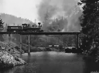 A Train Is Going Over A Bridge Over A River In A Black And White Photo . GIF
