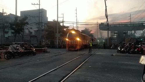 A Train Is Going Over A Railroad Crossing With A Sign That Says " Ayunan " In The Background GIF