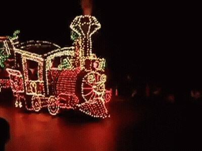 A Train With Christmas Lights On It Is Driving Down A Street GIF