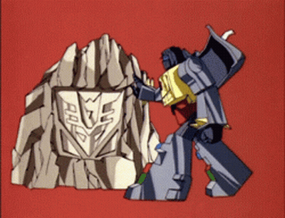 A Transformer Is Standing Next To A Rock With A Shield On It GIF
