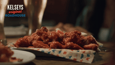 A Tray Of Chicken Wings Sits On A Table With A Sign That Says Kelseys Original Roadhouse GIF