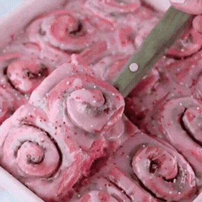 A Tray Of Pink Cinnamon Rolls With A Knife In It . GIF