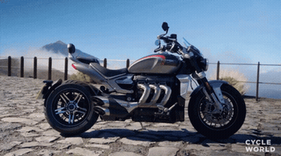 A Triumph Motorcycle Is Parked In Front Of A Mountain GIF