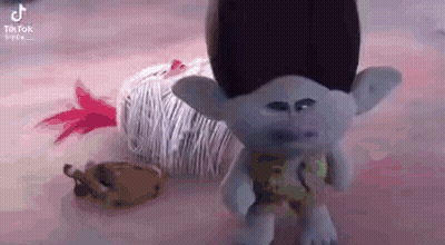 A Troll Doll Is Standing Next To A Ball Of Yarn On A Table . GIF