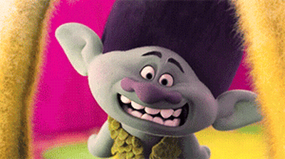 A Troll With A Purple Nose Is Smiling And Wearing A Green Scarf GIF
