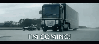A Truck Is Driving Down A Road Next To A Race Car . GIF