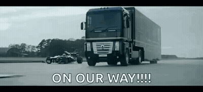 A Truck Is Driving Down A Road Next To A Race Car With The Words `` On Our Way !!! '' Written On It . GIF
