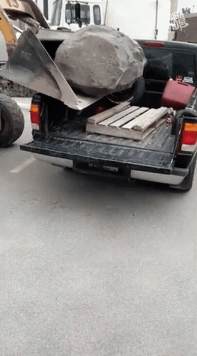 A Truck With A Large Rock In The Back Is Parked On A Street GIF