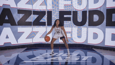 A Uconn Basketball Player Dribbles A Ball In Front Of A Large Screen That Says Azzi Fudd GIF