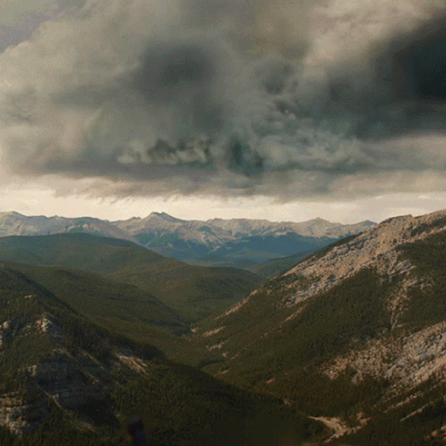 A Valley With Mountains In The Background And A Cloudy Sky In The Background GIF
