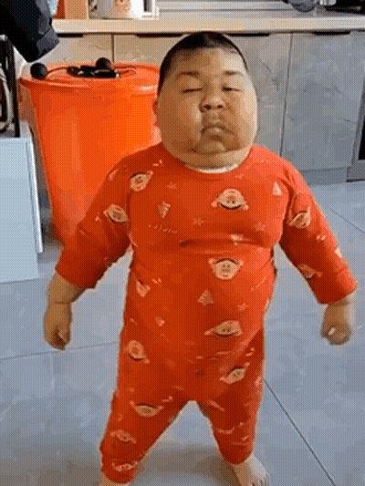 A Very Fat Baby In A Red Pajamas Is Standing On A Tiled Floor In A Kitchen . GIF