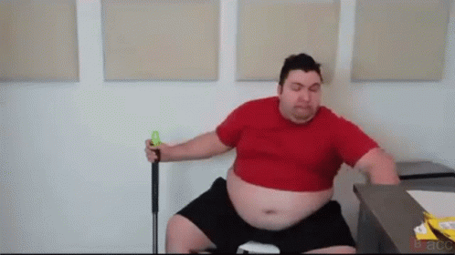 A Very Fat Man In A Red Shirt Is Sitting On A Chair Holding A Golf Club . GIF