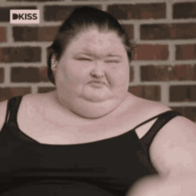 A Very Fat Woman Wearing A Black Tank Top Is Sitting In Front Of A Brick Wall GIF